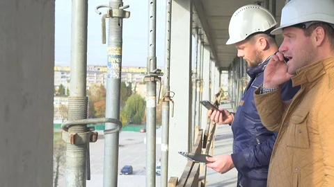 Two engineers browsing and talking by smartphone at builiding construction. Vídeos de archivo 72360421