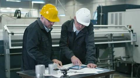 Two engineers discuss a blueprint while checking information on tablet computer Stock Footage