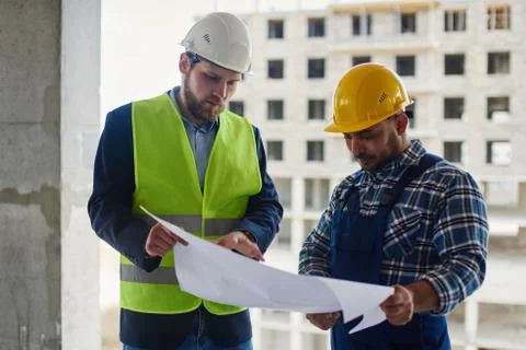 Two engineers discuss drafts they both hold. Stock Photos