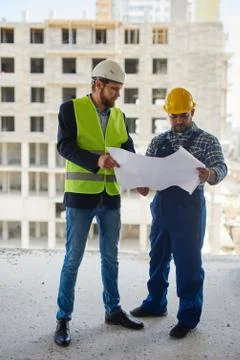 Two engineers discuss drafts they both hold. Stock Photos