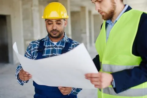 Two engineers discuss drafts they both hold. Stock Photos