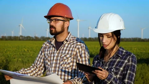 Two engineers discuss on plan on big piece of paper while walking in a field Stock Footage 96842786
