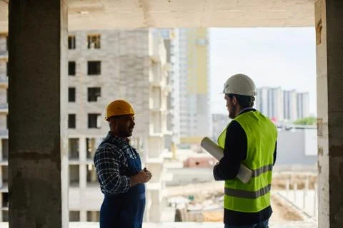 Two engineers discuss work related questions together holding folded blueprint. Stock Photos