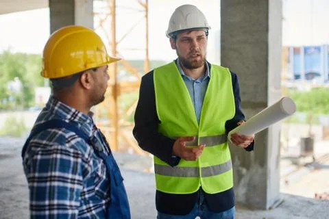 Two engineers discuss work related questions together holding folded blueprint. Stock Photos