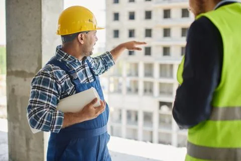 Two engineers discuss work related questions together holding folded blueprint. Stock Photos