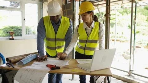 Two engineers discussing site plan while electricians working behind at site Stock Footage 108187169