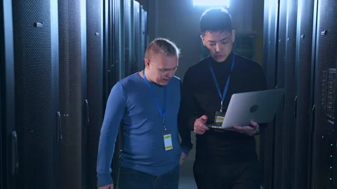 Two engineers doing network diagnostics on digital laptop and talking, walking Stock Footage 163631230