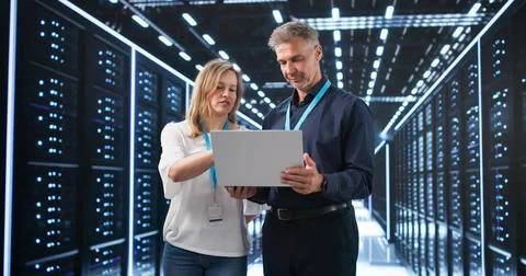Two Engineers Examine Data Servers In A Busy Secure Technology Center Room. Stock Photos