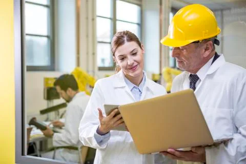 Two engineers in factory with tablet and laptop Stock Photos