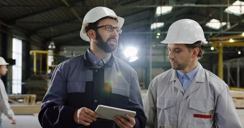 Two engineers in helmets with a tablet computer walking and discussing their Stock Footage 84423732