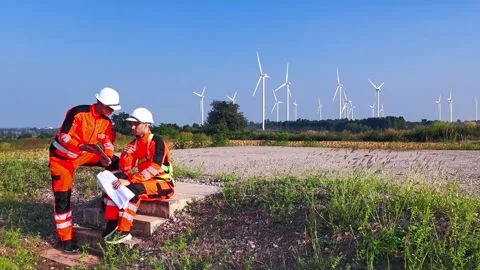 Two engineers in high-visibility gear review site plans at a wind farm Stock Footage 330159412