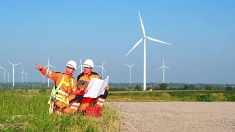 Two engineers in high-visibility gear review plans and point across a wind .. Stock Footage 330159432