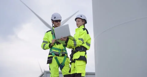 Two engineers in high visibility uniform using laptop near wind turbine, Video stock 321792388