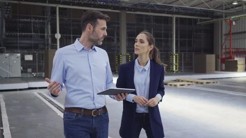 Two engineers looking at tablet and talking while walking in factory hall Stock Footage 108446034
