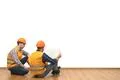 The two engineers with a paper sit on the floor on the white wall background Photo