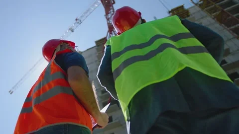 Two engineers in protective helmets standing  in front of unfinished building Vídeos de archivo 148355982