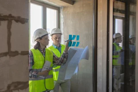 Two engineers in protective vests and white helmets glue stickers on the window Stock Photos
