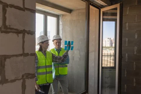 Two engineers in protective vests and white helmets glue stickers on the window Stock Photos