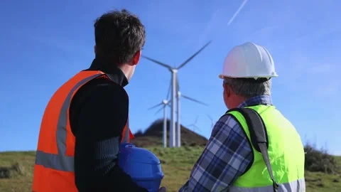 Two engineers, seen from behind, discussing wind turbine functionality in fie Stock Footage 294975827