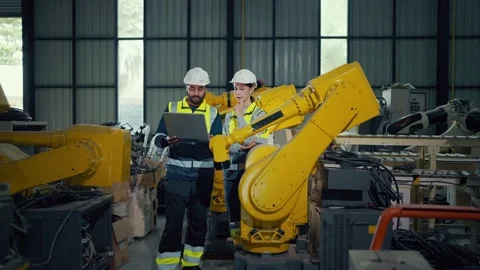Two engineers stand beside a large yellow robotic arm Video stock 340987680