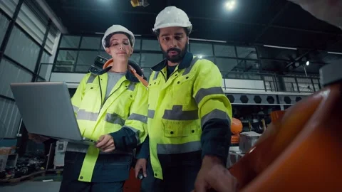 Two engineers stand beside an orange robotic arm Stockbeeldmateriaal 340982593