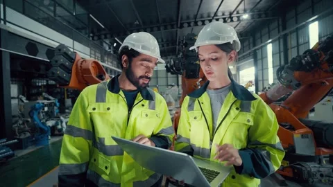 Two engineers stand beside an orange robotic arm Video stock 340982632
