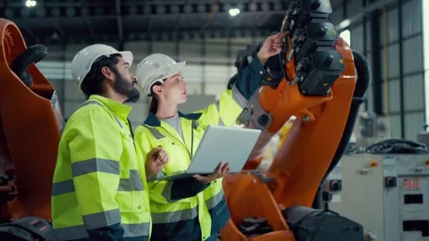 Two engineers stand beside an orange robotic arm Video stock 340982673