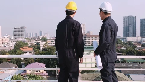 Two engineers stand on the roof of construction site looking to city Video stock 129584920