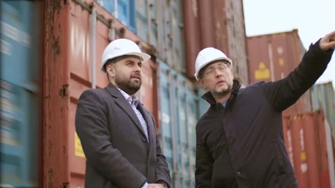 Two engineers supervise the loading of a container onto a cargo ship for Stock Footage 306217385