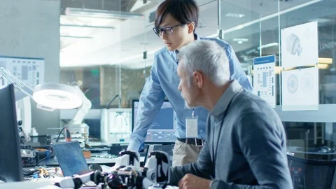 Two Engineers Talking while Working with Robot, Checking Data on Laptop Computer Stock Footage 85771058
