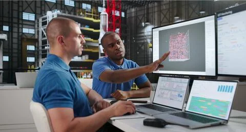 Two Engineers Use Laptops Designing Rocket Parts In Aerospace Lab. Stock Photos