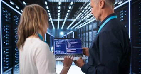Two Engineers Use Laptops To Manage Cloud Servers And Ensure Security. Stockfoto's