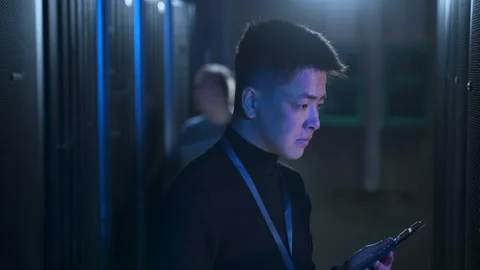 Two engineers using devices and doing network diagnostics while standing in data Stock Footage 168515774