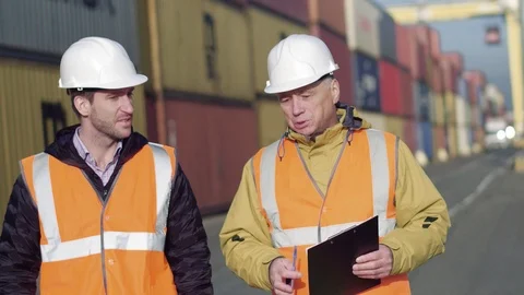 Two engineers wearing hardhats standing on a large commercial shipping dock Stock Footage 101230246