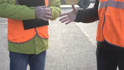 Two engineers wearing orange workwear meeting to skake hands on a large Stock Footage 101231750