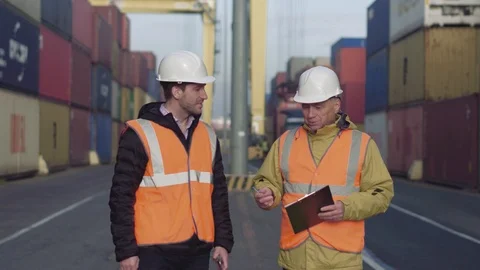 Two engineers wearing white hardhats walking on a large commercial dock Video stock 101230769
