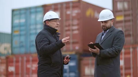 Two engineers in white helmets supervise loading at a container yard for Stock Footage 142376323