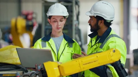 Two engineers work closely beside a yellow robotic arm Stock Footage 347352268