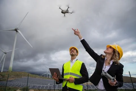 Two engineers at work fly a drone and use the laptop in a solar farm with w.. Stock Photos