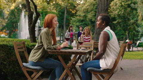 Two enthralling looking women are at a table outside surrounded by trees and Video stock 160976063
