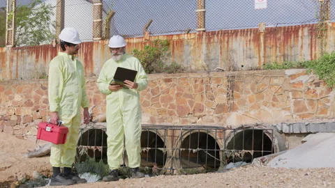 Two environmental engineers in protective suits inspect a wastewater outlet Stock Footage 336892041
