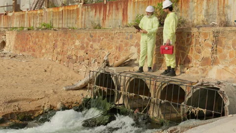 Two environmental scientists in hazmat suits inspect a sewer outfall Vídeo Stock 346080180