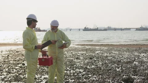 Two environmental scientists in protective gear inspect a coastal area near an Stock Footage 334946137