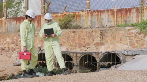 Two environmental scientists in protective gear inspect a sewer outfall Stock Footage 336891767