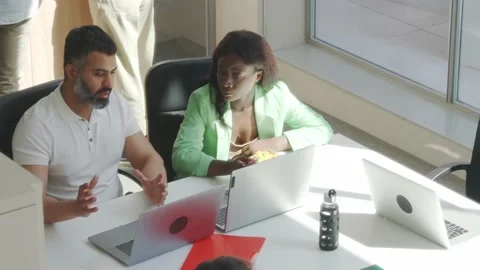 Two ethnic workers in an office talking while they work and eat. Stock Footage 166576201