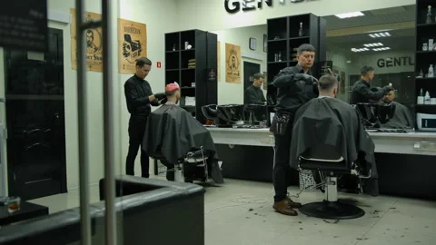 Two experienced masters in black gloves make haircuts to customer in barbershop Vidéo 134272997