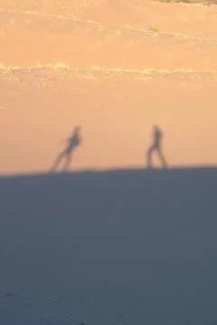 Two explorers on the desert, casting shadows on the sand dunes on a hot, sunny d Stock Photos