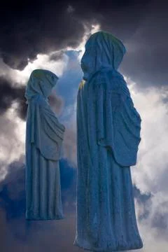 Two faceless monk statues against dark skies Stock Photos
