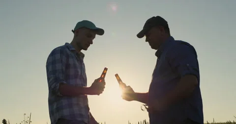 Two farmer men open beer bottles, clink glasses and drink. Stock Footage 251348719