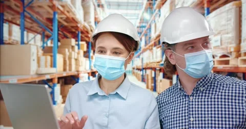 Two fellow managers in protective helmets and masks stand in warehouse and work Stock Footage 151780474